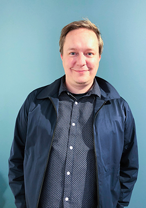 Kuvassa AVEKissa elokuussa aloittanut tuotantoneuvoja Mikko Peltonen. Hän seisoo vasten sinistä seinää, katsoo suoraan kameraan ja hymyilee.