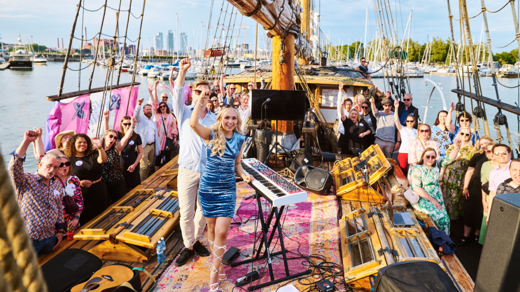 Crowd of people standing on the deck of the sailing boat with hands up.