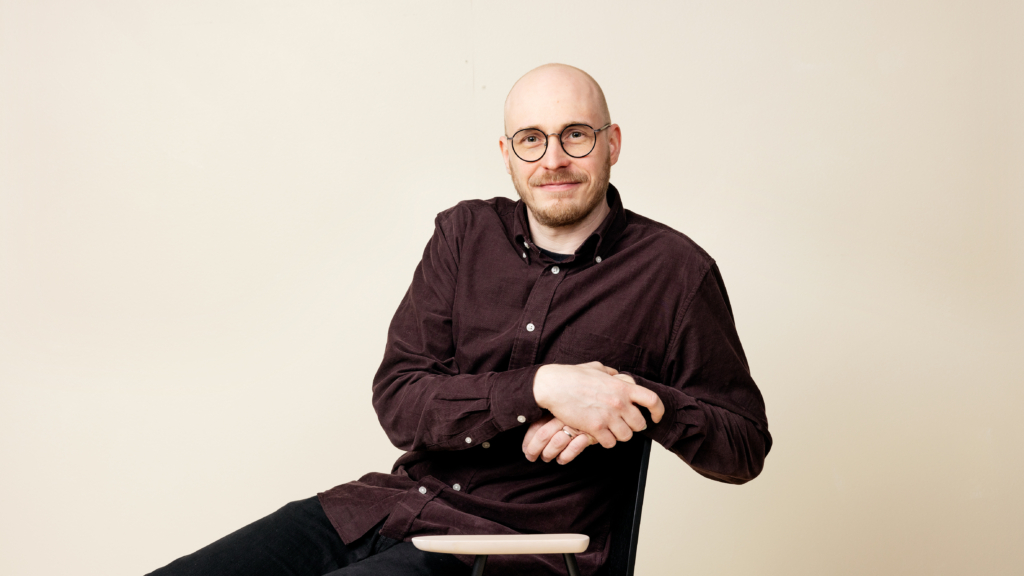 Niko Tuomonen istuu tuolilla ja katsoo kameraan hymyillen.