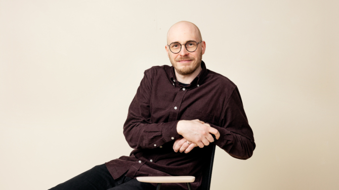 Niko Tuomonen istuu tuolilla ja katsoo kameraan hymyillen.