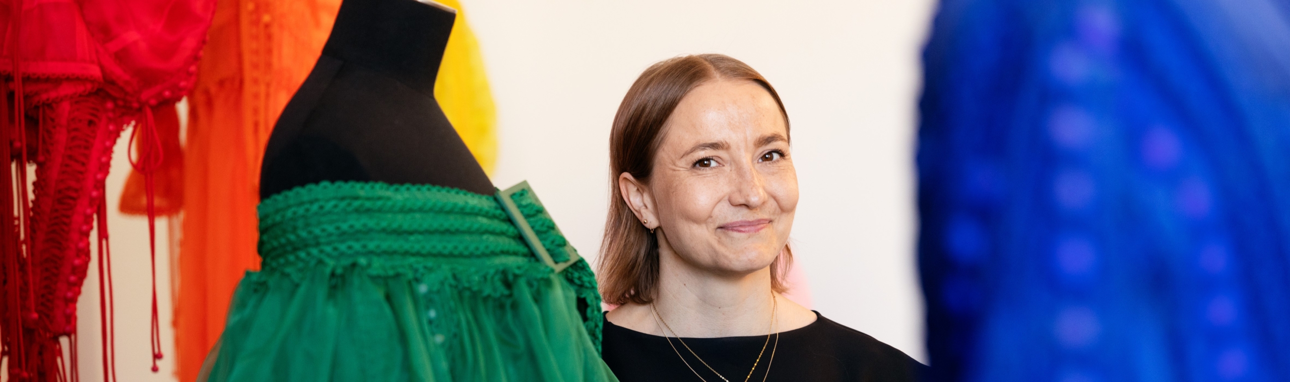 Sofia Ilmonen hymyilee kameralle. Ympärillä kaksi mallinukkea.