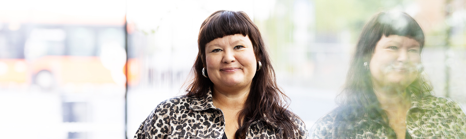 Susse Roos looks at the camera and smiles. Windows in the background.