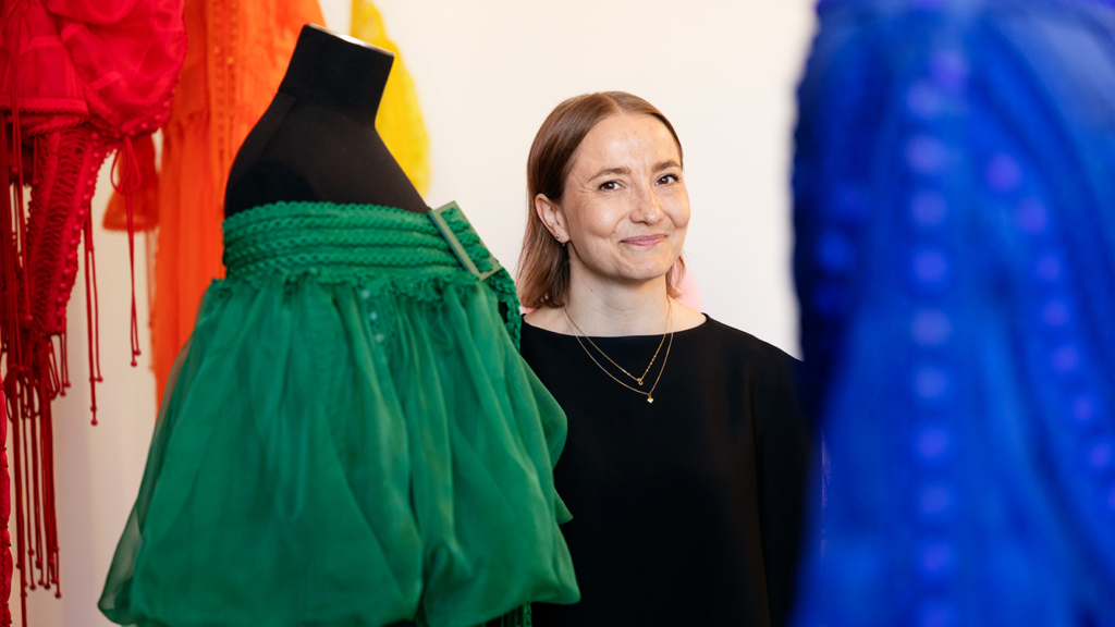 Sofia Ilmonen hymyilee kameralle. Ympärillä kaksi mallinukkea.