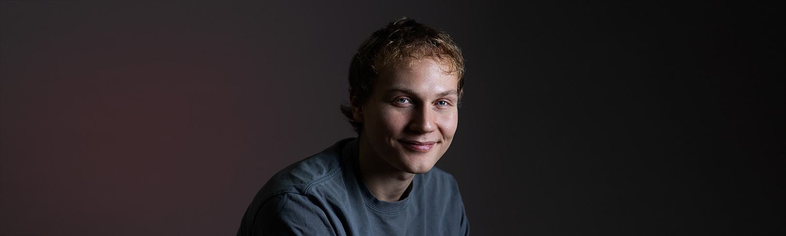 Elias Salonen smiling. Dark background.