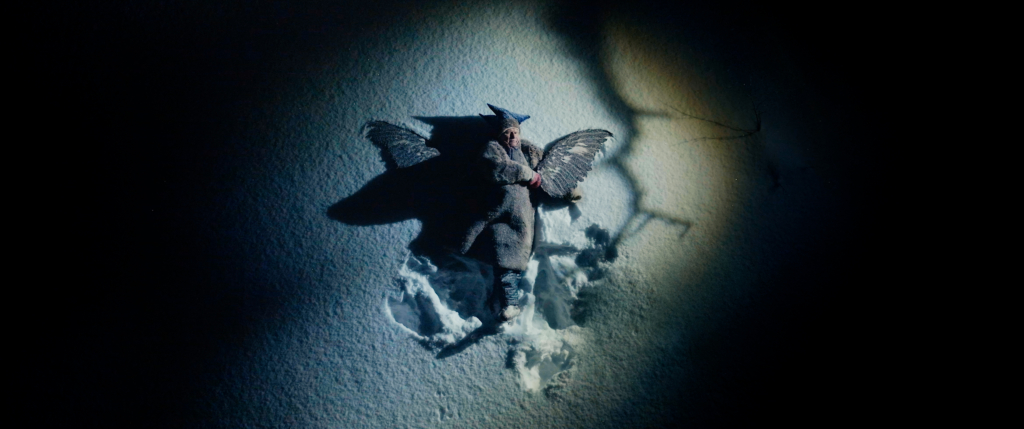 A man lying in the snow. Wings on his back. Darkness around him.
