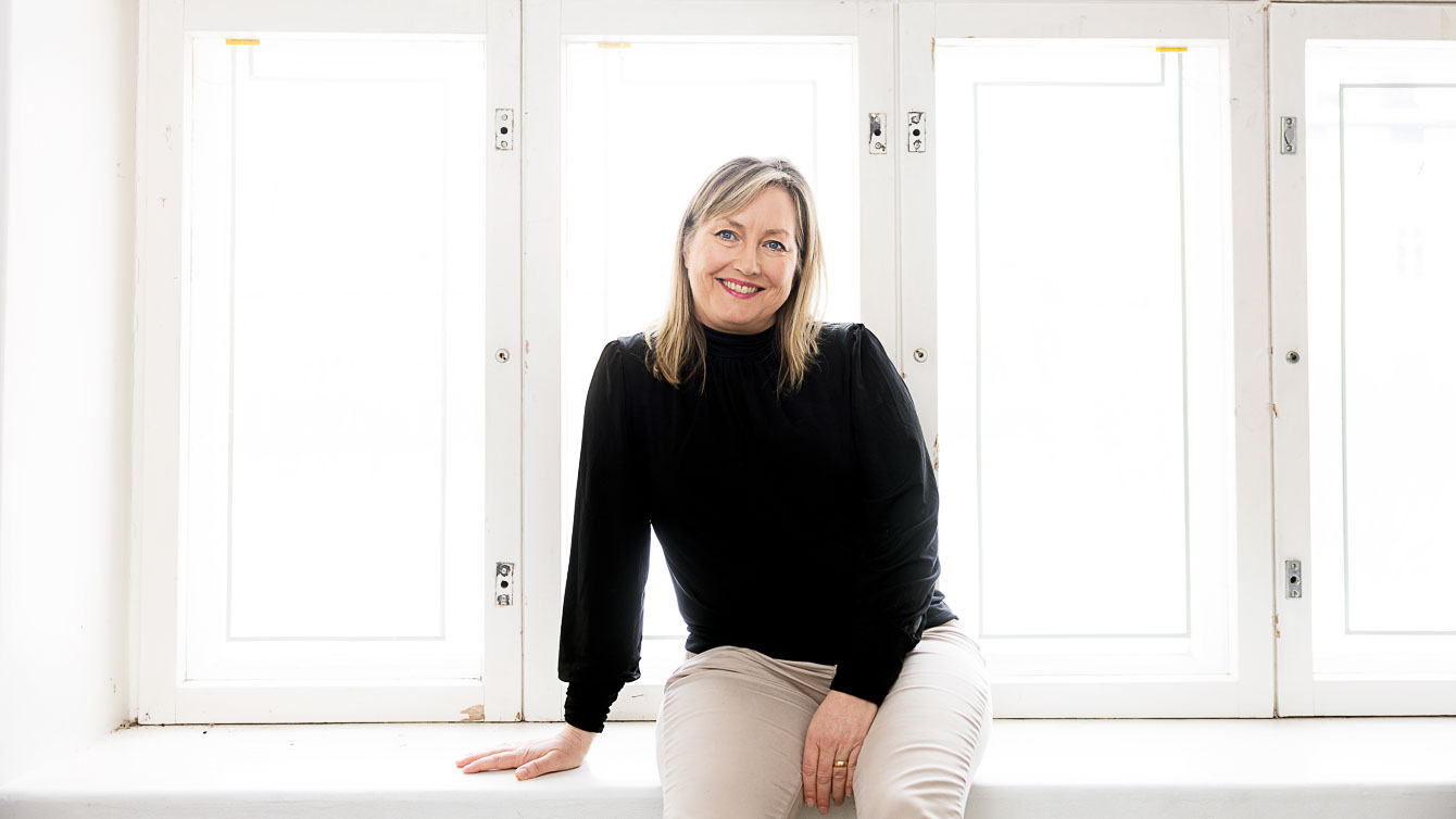 Anna Blom istuu ikkunnalaudalla, katsoo kameraan hymyillen.
